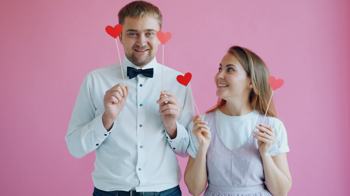 Pembe fon önünde kalp aksesuarlarıyla poz veren çift: photobooth köşesinde eğlenceli çekim